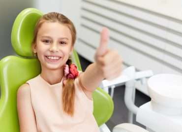 Portrait of happy girl shows thumb up gesture at dental clinic
